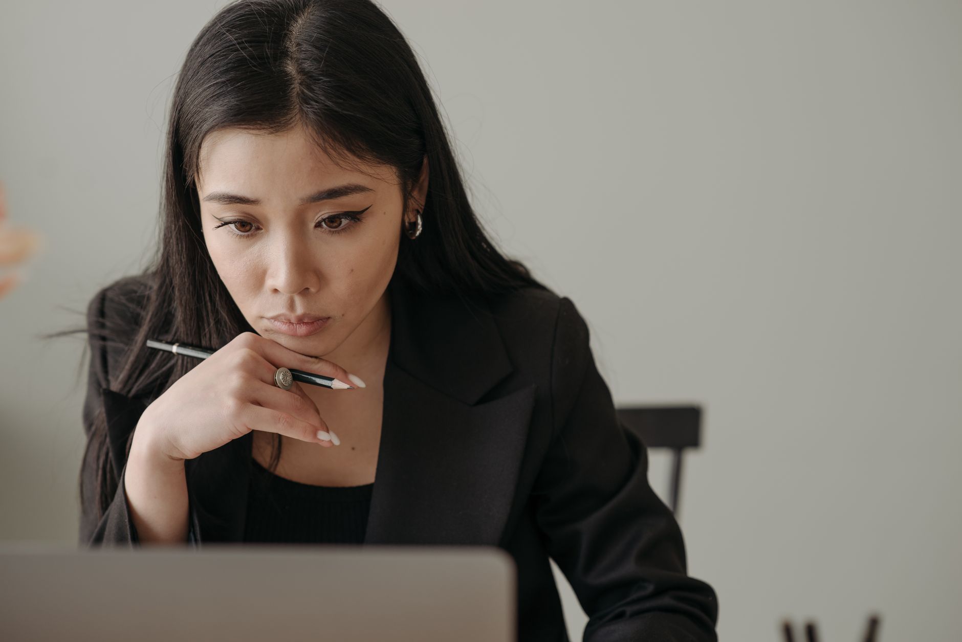 Young woman working remotely, focused on laptop in home office, holding a pencil.