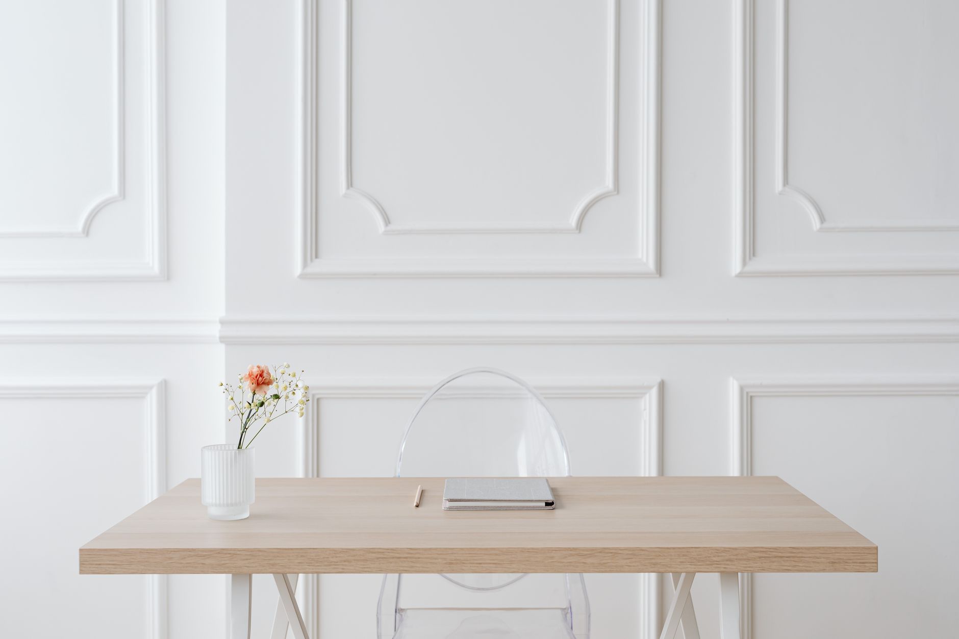 Elegant minimalist workspace with wooden desk, glass vase and panel wall.